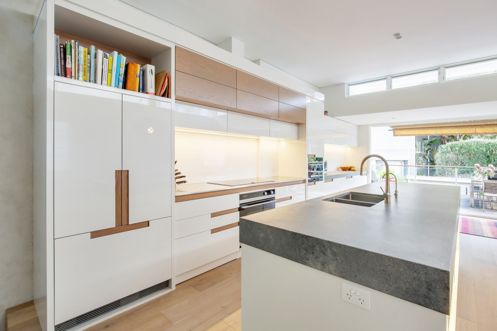 Inspiration for a modern galley kitchen in Sydney with an undermount sink, flat-panel cabinets, white cabinets, panelled appliances, light hardwood floors, with island, beige floor and grey benchtop.