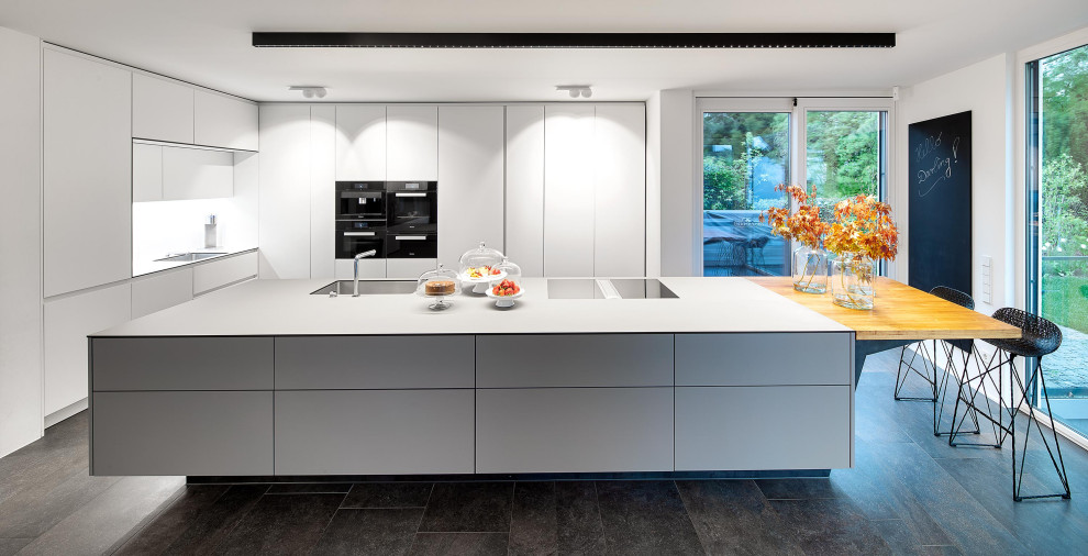 This is an example of a large contemporary eat-in kitchen in Stuttgart with flat-panel cabinets, white cabinets, with island, grey benchtop and black floor.