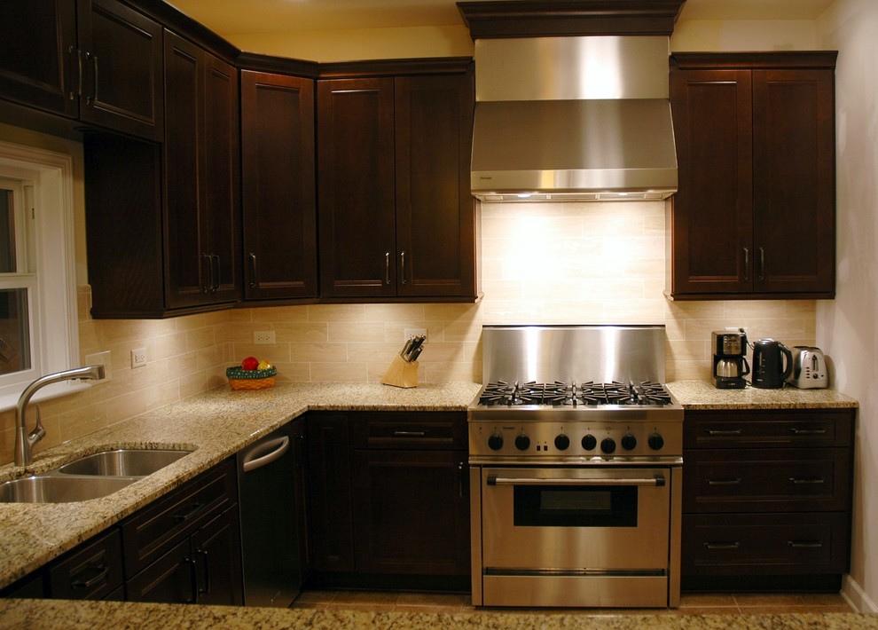 Example of a transitional u-shaped eat-in kitchen design with an undermount sink, recessed-panel cabinets, dark wood cabinets, granite countertops, beige backsplash, stone tile backsplash and stainless steel appliances