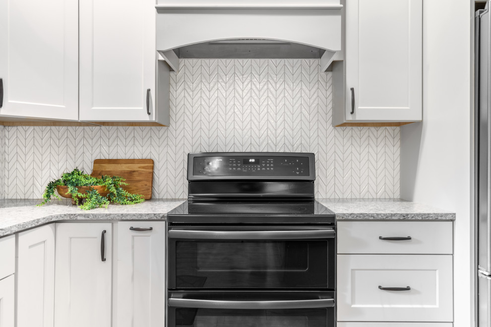 Example of a transitional l-shaped kitchen design in Minneapolis with an undermount sink, shaker cabinets, white cabinets, granite countertops, white backsplash, ceramic backsplash, stainless steel appliances, an island and gray countertops