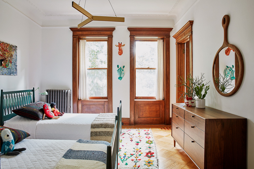 This is an example of a mid-sized transitional gender-neutral kids' bedroom for kids 4-10 years old in New York with white walls and medium hardwood floors.