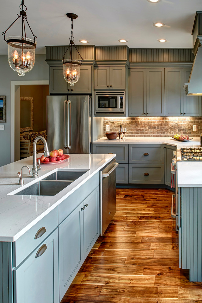 Eat-in kitchen - mid-sized transitional l-shaped medium tone wood floor eat-in kitchen idea with an undermount sink, recessed-panel cabinets, gray cabinets, quartz countertops, brown backsplash, brick backsplash, stainless steel appliances and an island