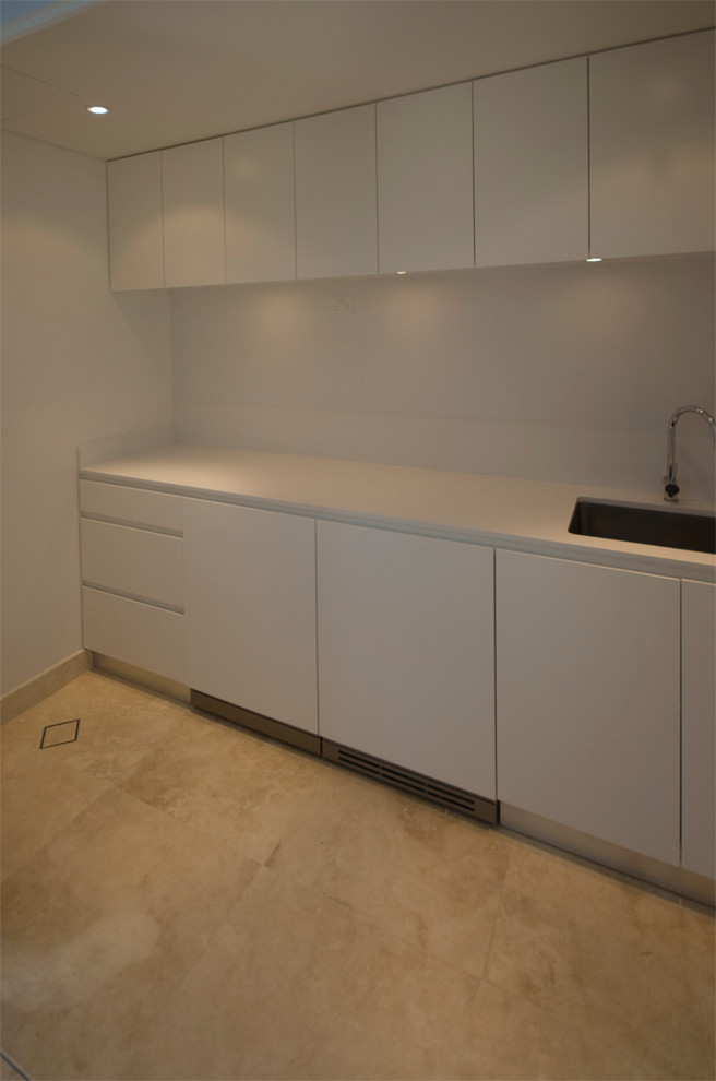 Photo of a modern laundry room in Sydney with an undermount sink, white cabinets, quartz benchtops, white walls and a concealed washer and dryer.