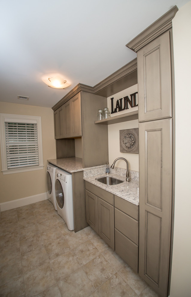 Photo of a mid-sized transitional single-wall dedicated laundry room in Boston with an undermount sink, a side-by-side washer and dryer, recessed-panel cabinets, beige cabinets, granite benchtops, beige walls, ceramic floors, beige floor and grey benchtop.