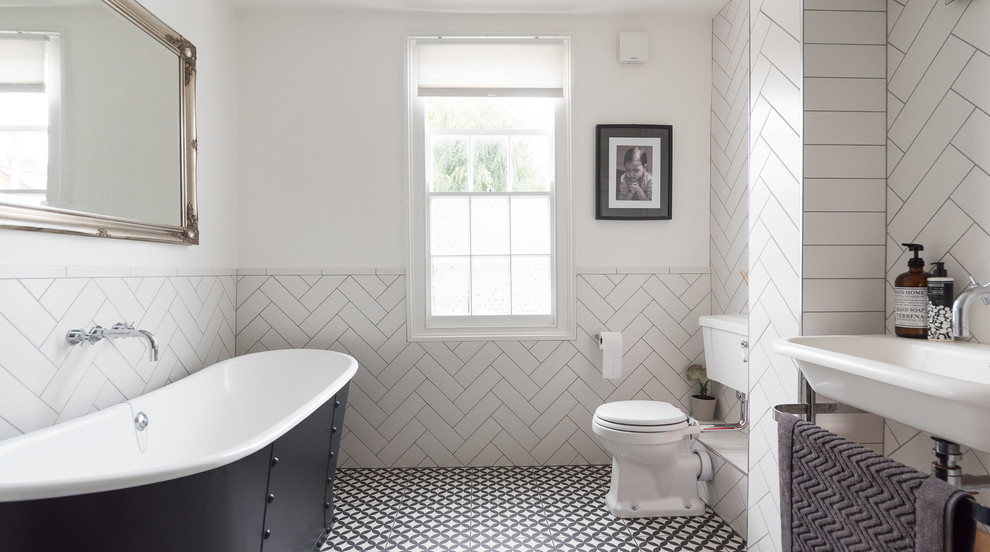 Photo of a mid-sized transitional bathroom in London with a freestanding tub, a two-piece toilet, white walls, white tile, a console sink and multi-coloured floor.