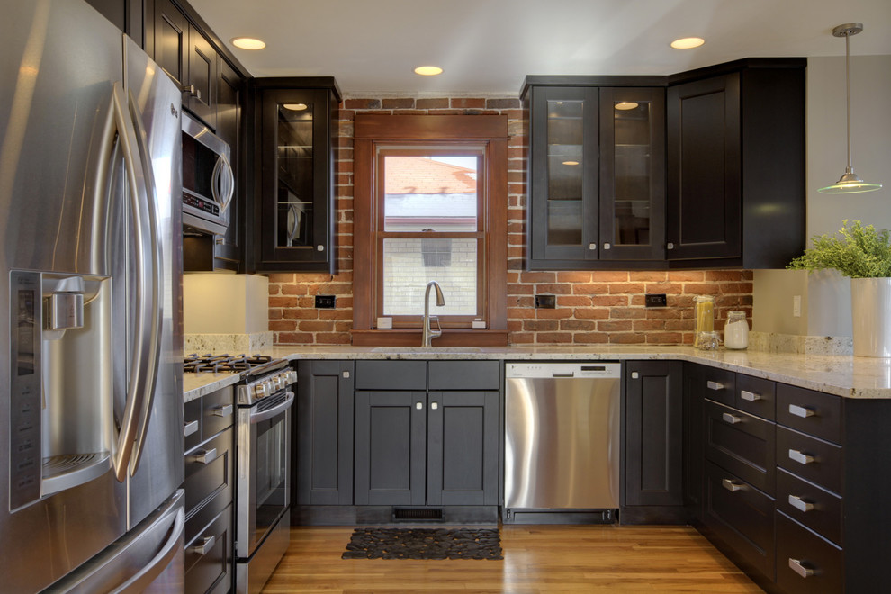 Design ideas for a mid-sized eclectic eat-in kitchen in Denver with shaker cabinets, red splashback, brick splashback, stainless steel appliances, light hardwood floors, a peninsula, brown floor and black cabinets.
