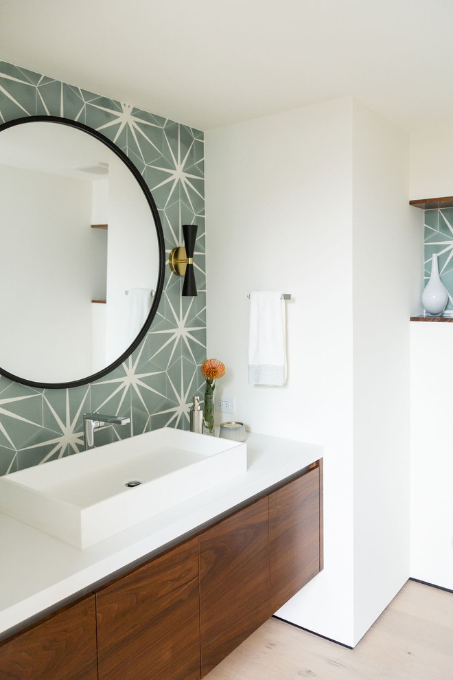 This is an example of a mid-sized modern powder room in San Diego with flat-panel cabinets, medium wood cabinets, green tile, cement tile, white walls, light hardwood floors, a vessel sink, engineered quartz benchtops, brown floor and white benchtops.