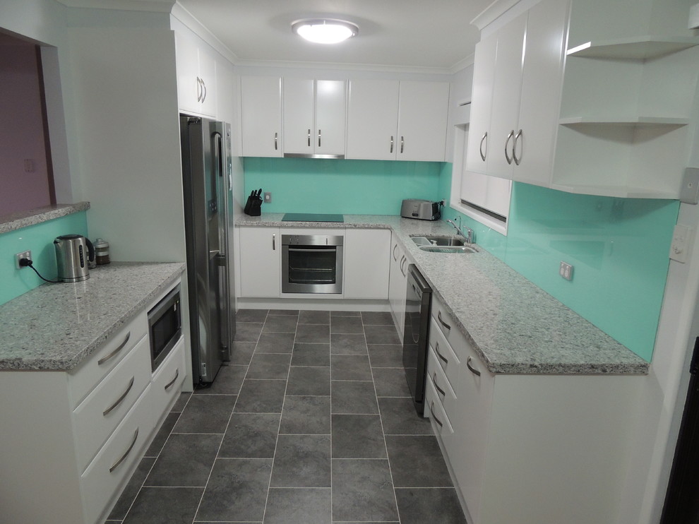 This is an example of a contemporary u-shaped eat-in kitchen in Brisbane with an undermount sink, flat-panel cabinets, white cabinets, quartz benchtops, green splashback, glass sheet splashback, stainless steel appliances and linoleum floors.