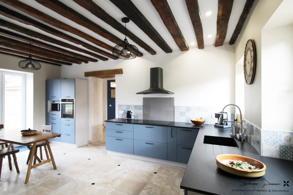Lantlig inredning av ett avskilt, stort svart svart l-kök, med en integrerad diskho, granitbänkskiva, blått stänkskydd, svarta vitvaror, travertin golv och beiget golv