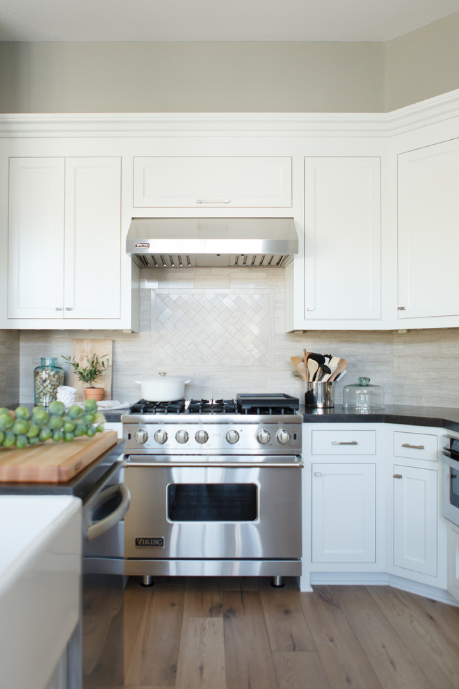 Large transitional l-shaped light wood floor open concept kitchen photo in Orange County with a farmhouse sink, beaded inset cabinets, white cabinets, beige backsplash, stone tile backsplash, stainless steel appliances, gray walls and an island