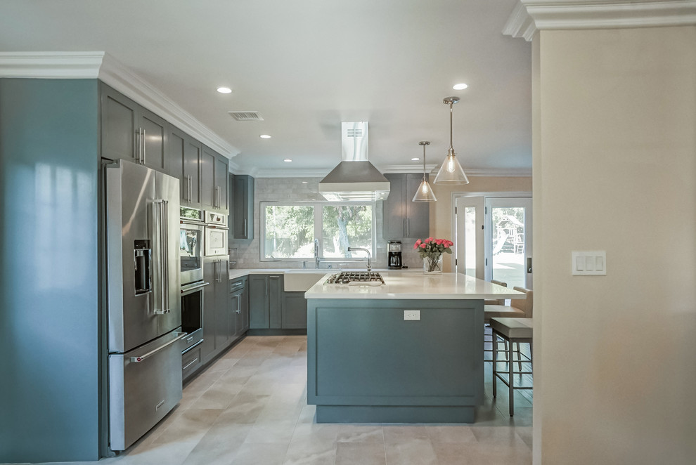 Large transitional l-shaped open plan kitchen in Los Angeles with a farmhouse sink, shaker cabinets, grey cabinets, quartz benchtops, grey splashback, marble splashback, stainless steel appliances, porcelain floors, with island and white floor.