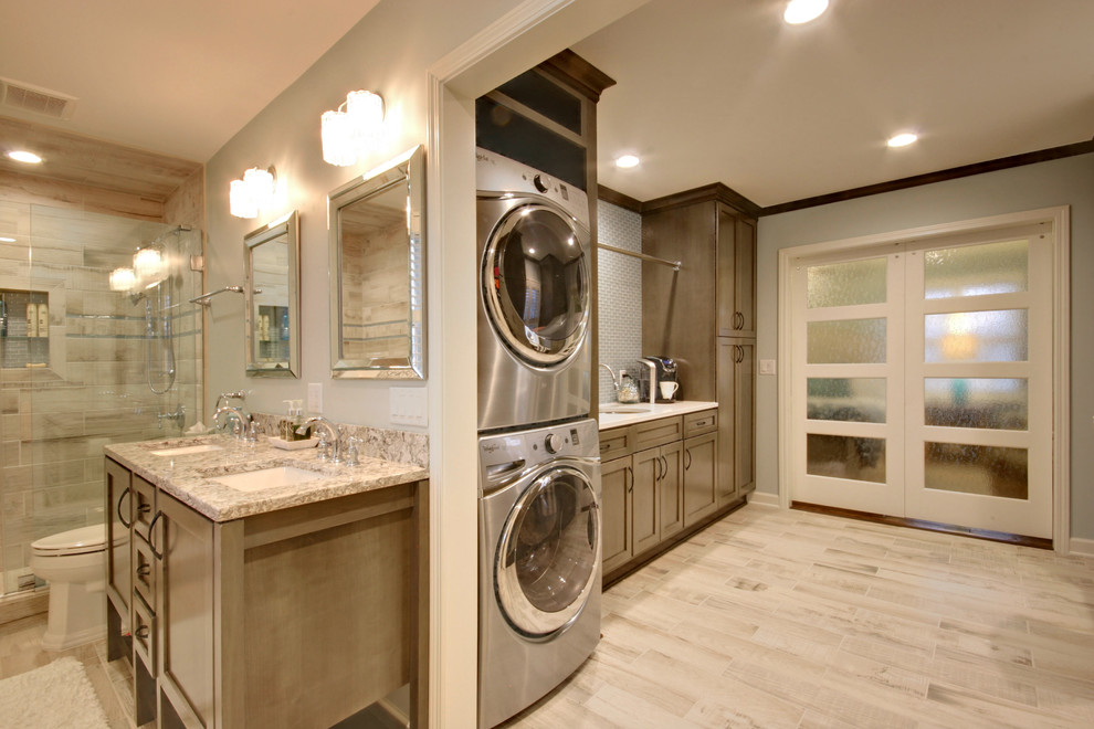 Inspiration for an expansive transitional galley utility room in Grand Rapids with an undermount sink, recessed-panel cabinets, grey cabinets, onyx benchtops, ceramic floors, a stacked washer and dryer, grey floor and grey walls.