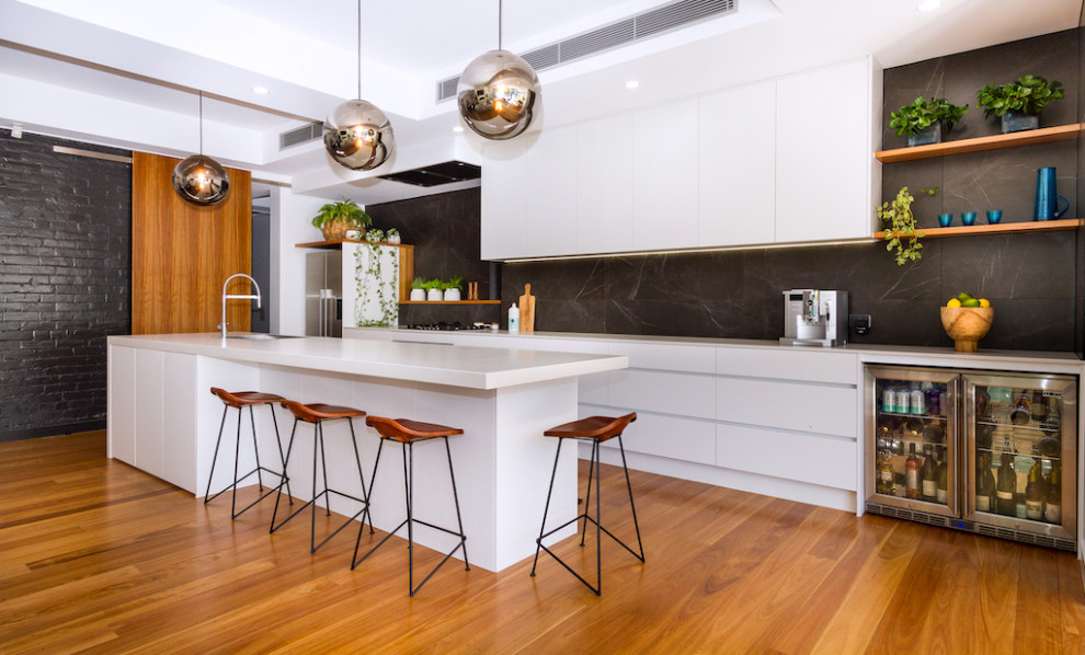 Inspiration for an expansive contemporary galley open plan kitchen in Brisbane with a drop-in sink, flat-panel cabinets, quartz benchtops, black splashback, marble splashback, stainless steel appliances, medium hardwood floors, with island, brown floor and white cabinets.