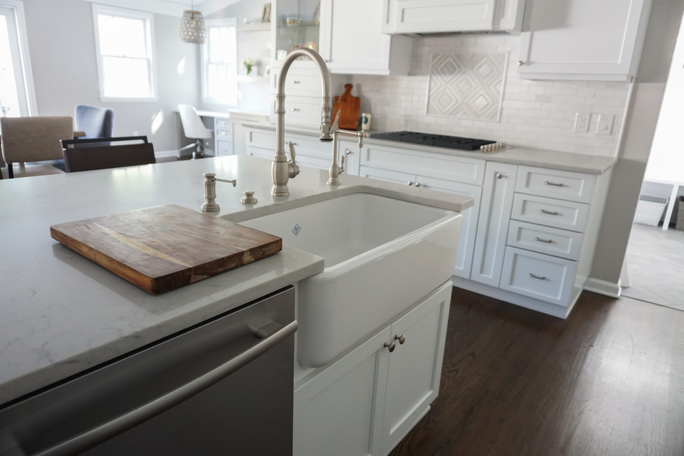 Inspiration for a mid-sized transitional galley eat-in kitchen in New York with a farmhouse sink, shaker cabinets, white cabinets, quartz benchtops, white splashback, stone tile splashback, stainless steel appliances, dark hardwood floors and with island.