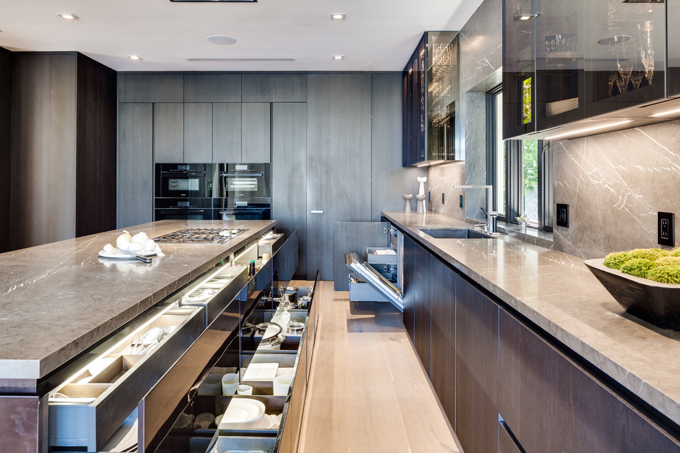 Photo of a large contemporary single-wall open plan kitchen in Miami with flat-panel cabinets, blue cabinets, grey splashback, stone slab splashback, black appliances, light hardwood floors, with island, beige floor and beige benchtop.