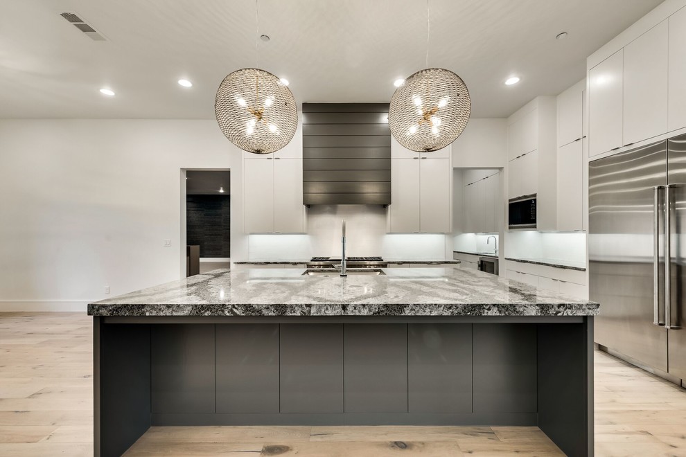This is an example of a large contemporary l-shaped kitchen/diner in Dallas with a submerged sink, flat-panel cabinets, white cabinets, engineered stone countertops, white splashback, metro tiled splashback, stainless steel appliances, light hardwood flooring, an island and multi-coloured floors.