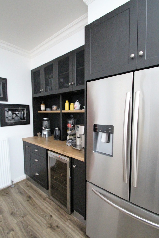 This is an example of a mid-sized country l-shaped eat-in kitchen in Other with a farmhouse sink, shaker cabinets, black cabinets, laminate benchtops, multi-coloured splashback, stone tile splashback, stainless steel appliances, vinyl floors, with island, grey floor and brown benchtop.