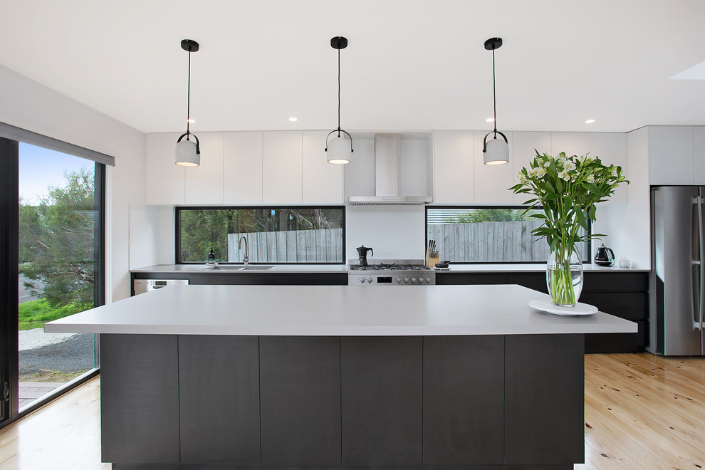 This is an example of a large contemporary single-wall kitchen in Other with an undermount sink, flat-panel cabinets, black cabinets, quartz benchtops, stainless steel appliances, with island, beige floor, window splashback and light hardwood floors.