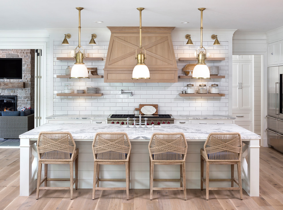 Inspiration for a beach style kitchen in Minneapolis with a farmhouse sink, shaker cabinets, white cabinets, marble benchtops, white splashback, subway tile splashback, stainless steel appliances, light hardwood floors, with island, beige floor and white benchtop.