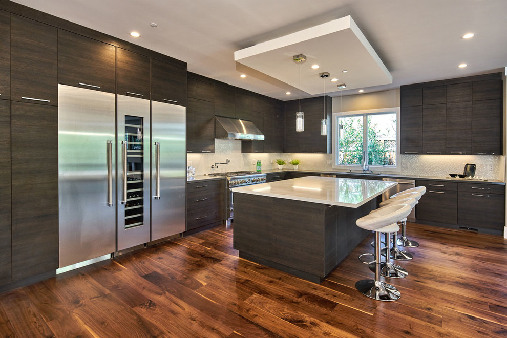 Photo of a large contemporary l-shaped open plan kitchen in San Francisco with an undermount sink, flat-panel cabinets, dark wood cabinets, quartz benchtops, white splashback, porcelain splashback, stainless steel appliances, dark hardwood floors and with island.