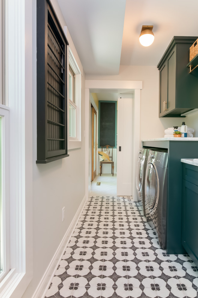 Inspiration for a transitional l-shaped utility room in New York with a drop-in sink, shaker cabinets, green cabinets, granite benchtops, grey walls, ceramic floors, a side-by-side washer and dryer, white floor and white benchtop.