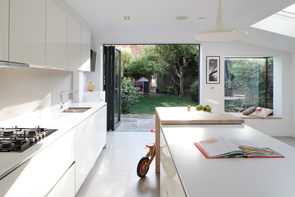 Inspiration for a mid-sized contemporary single-wall open plan kitchen in London with an integrated sink, flat-panel cabinets, white cabinets, solid surface benchtops, grey splashback, ceramic splashback, panelled appliances, ceramic floors, with island, grey floor, white benchtop and vaulted.