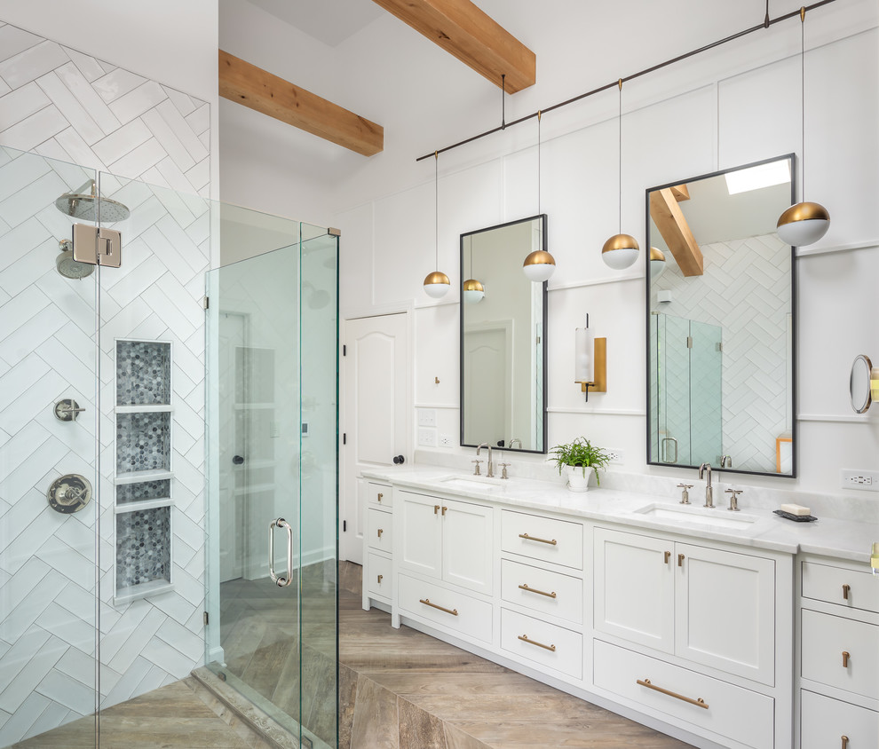 This is an example of a mid-sized country master bathroom in Raleigh with recessed-panel cabinets, white cabinets, a freestanding tub, a curbless shower, a two-piece toilet, white tile, ceramic tile, white walls, porcelain floors, an undermount sink, marble benchtops, brown floor, a hinged shower door and white benchtops.