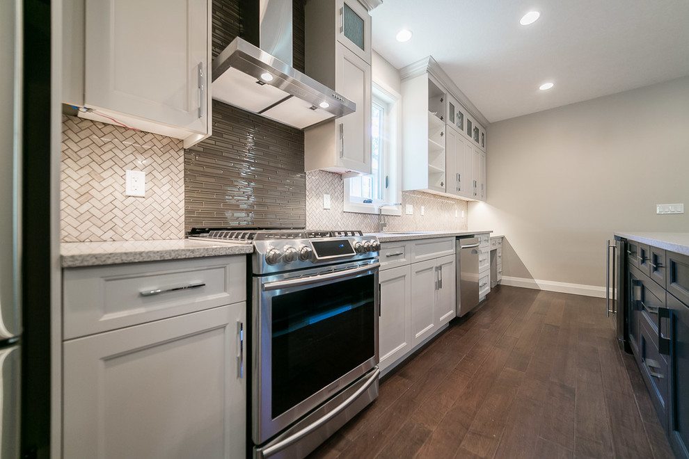 Example of a mid-sized transitional galley dark wood floor kitchen pantry design in Edmonton with shaker cabinets, white cabinets, multicolored backsplash, matchstick tile backsplash, stainless steel appliances, an island, an undermount sink and granite countertops