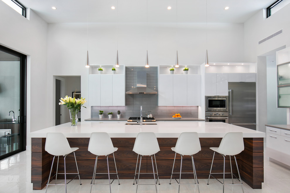 Design ideas for a large contemporary l-shaped open plan kitchen in Tampa with an undermount sink, flat-panel cabinets, white cabinets, quartz benchtops, grey splashback, glass tile splashback, stainless steel appliances, porcelain floors, with island, white floor and grey benchtop.