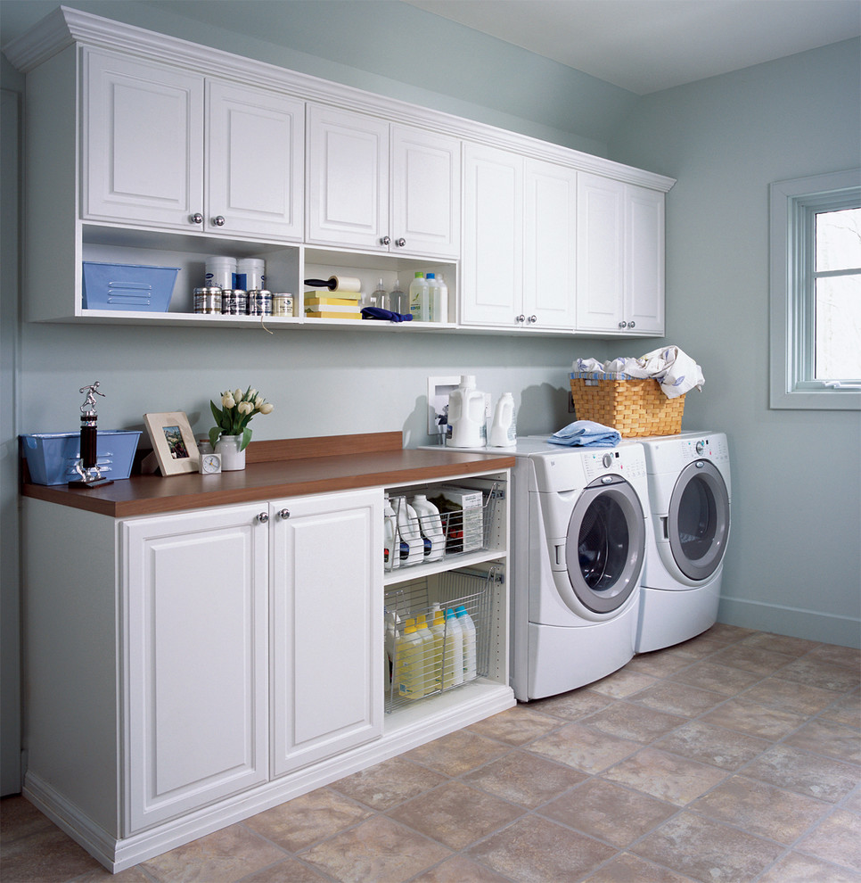 This is an example of a mid-sized contemporary single-wall utility room in New York with recessed-panel cabinets, white cabinets, wood benchtops, white walls, a side-by-side washer and dryer and ceramic floors.