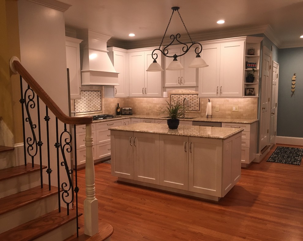 Example of a large transitional l-shaped medium tone wood floor and brown floor open concept kitchen design with an undermount sink, shaker cabinets, white cabinets, granite countertops, beige backsplash, subway tile backsplash, stainless steel appliances, an island and beige countertops