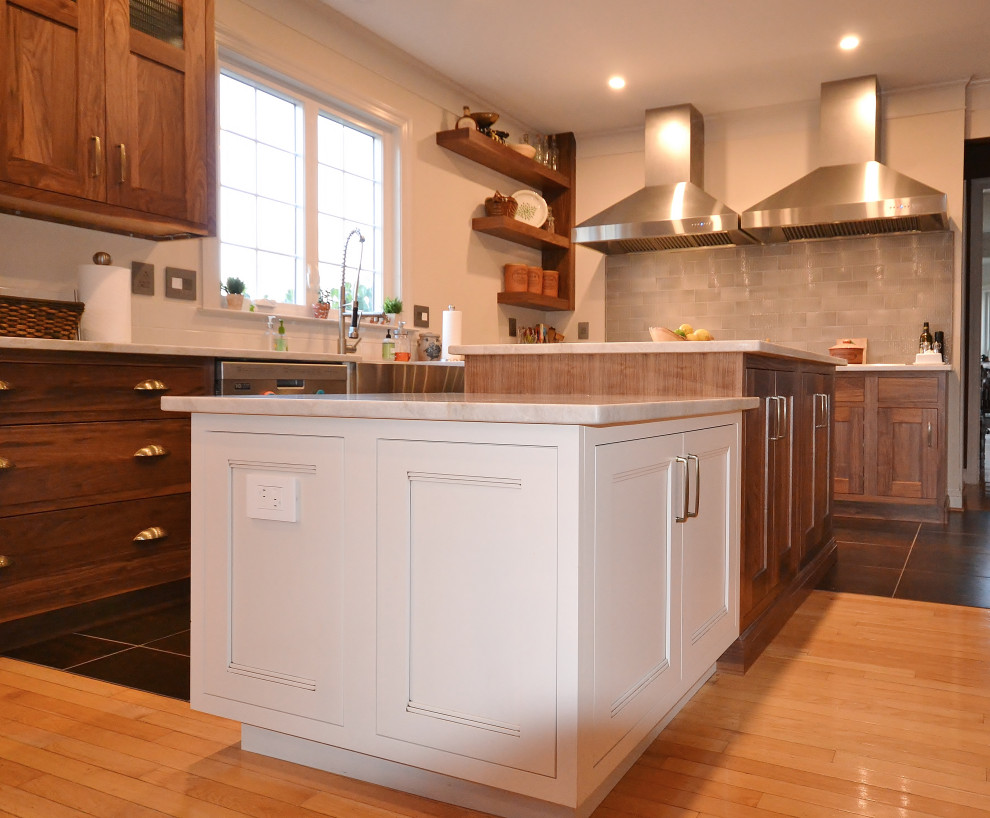 Photo of an expansive transitional l-shaped eat-in kitchen in Philadelphia with a farmhouse sink, raised-panel cabinets, medium wood cabinets, quartzite benchtops, grey splashback, subway tile splashback, stainless steel appliances, light hardwood floors, multiple islands, beige floor and white benchtop.