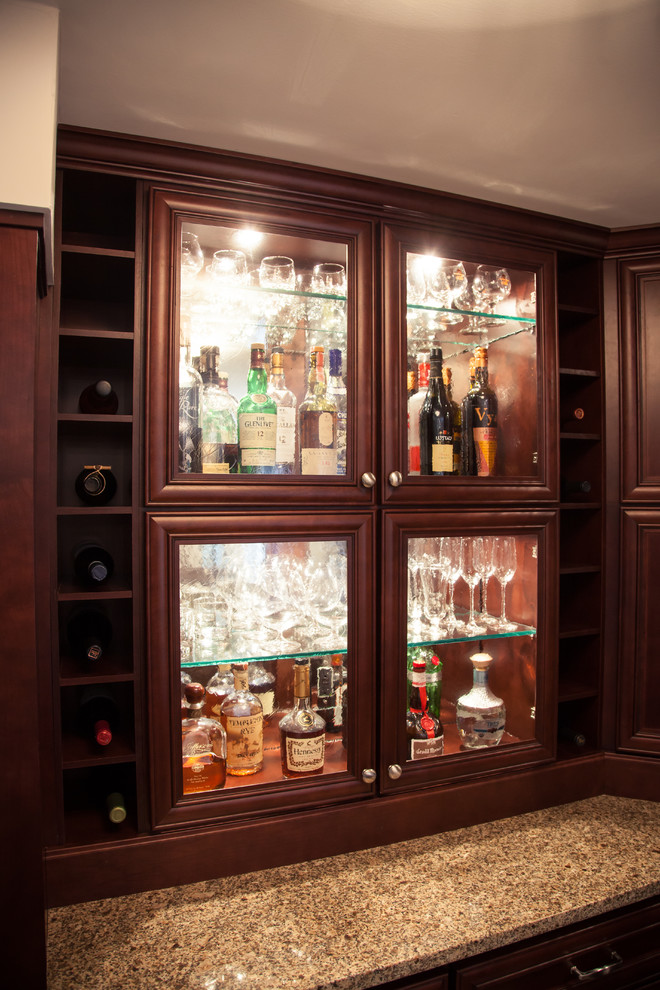 This is an example of a mid-sized traditional single-wall wet bar in Cincinnati with an undermount sink, raised-panel cabinets, dark wood cabinets, granite benchtops and porcelain floors.
