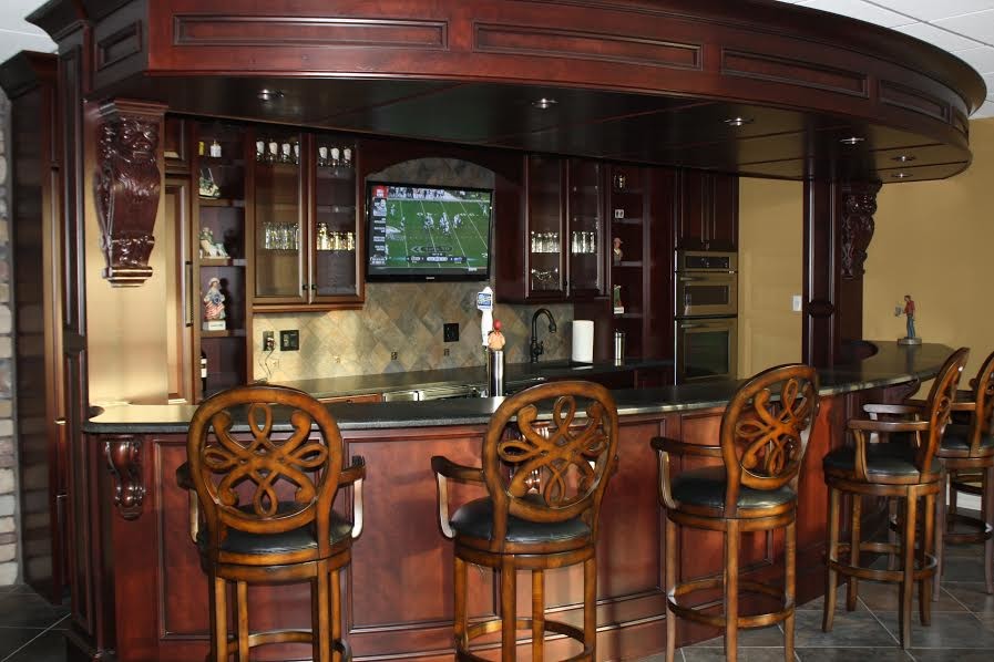 This is an example of a large arts and crafts galley seated home bar in Chicago with glass-front cabinets, dark wood cabinets, granite benchtops, multi-coloured splashback, stone tile splashback and terra-cotta floors.