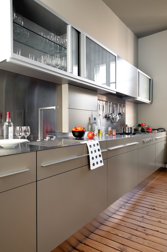 This is an example of a mid-sized contemporary galley separate kitchen in Bordeaux with an integrated sink, flat-panel cabinets, grey cabinets, stainless steel benchtops, metallic splashback, medium hardwood floors and no island.