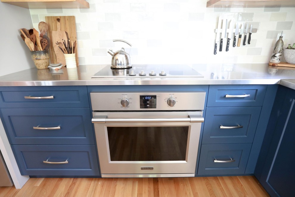 Mid-sized transitional l-shaped light wood floor and beige floor open concept kitchen photo with an integrated sink, shaker cabinets, blue cabinets, stainless steel countertops, ceramic backsplash, stainless steel appliances, an island and gray countertops