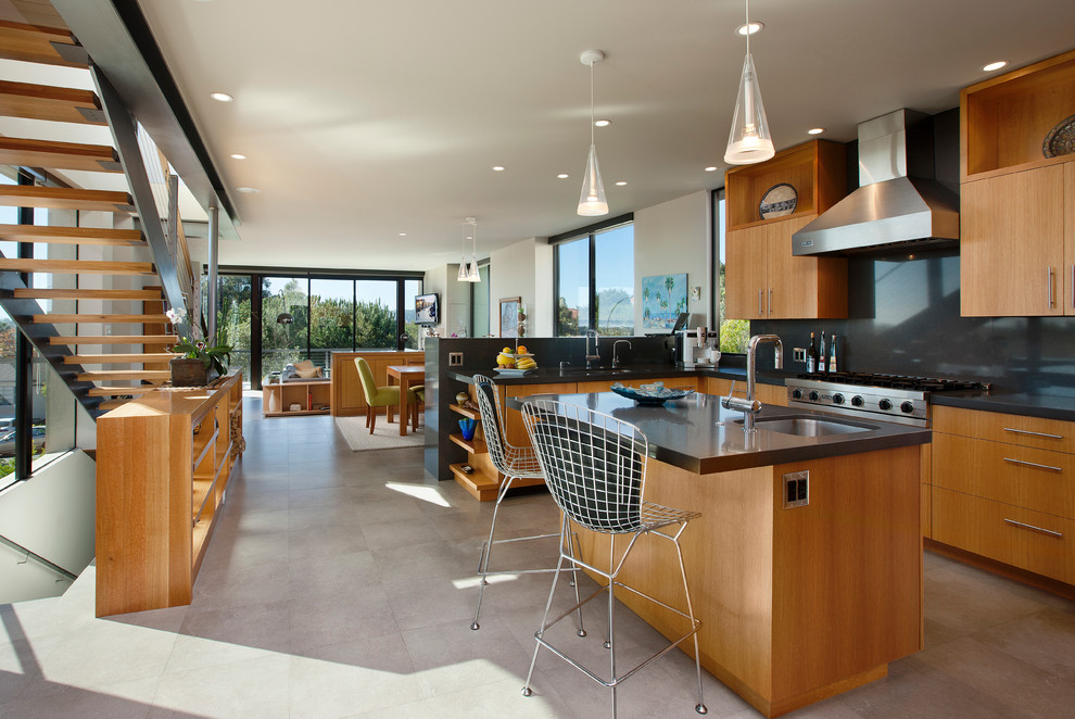 Photo of a contemporary open plan kitchen in Santa Barbara with with island, stainless steel appliances, an undermount sink, flat-panel cabinets, medium wood cabinets and black splashback.