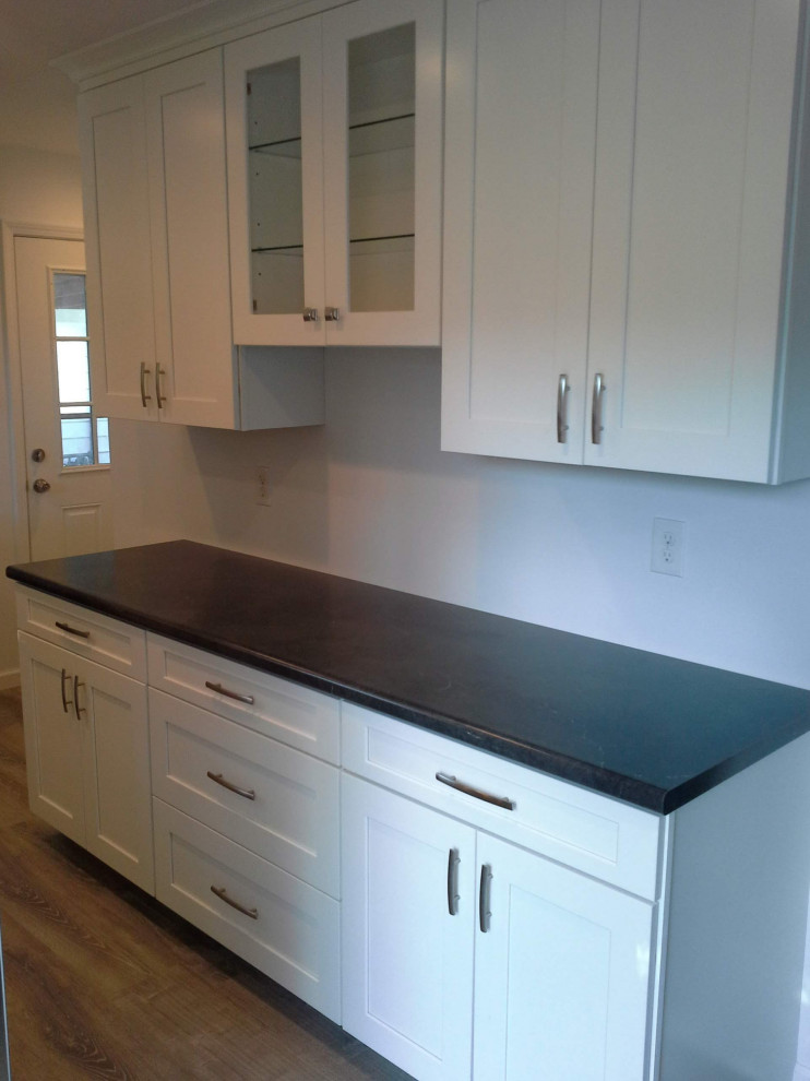 Inspiration for a mid-sized contemporary u-shaped kitchen in St Louis with shaker cabinets, white cabinets, laminate benchtops, stainless steel appliances, laminate floors, black benchtop and grey floor.