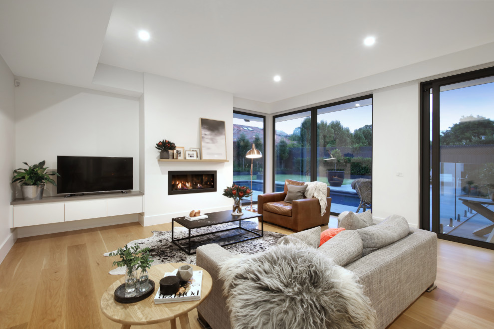 Inspiration for a contemporary open concept living room in Melbourne with white walls, light hardwood floors, a ribbon fireplace, a freestanding tv and beige floor.