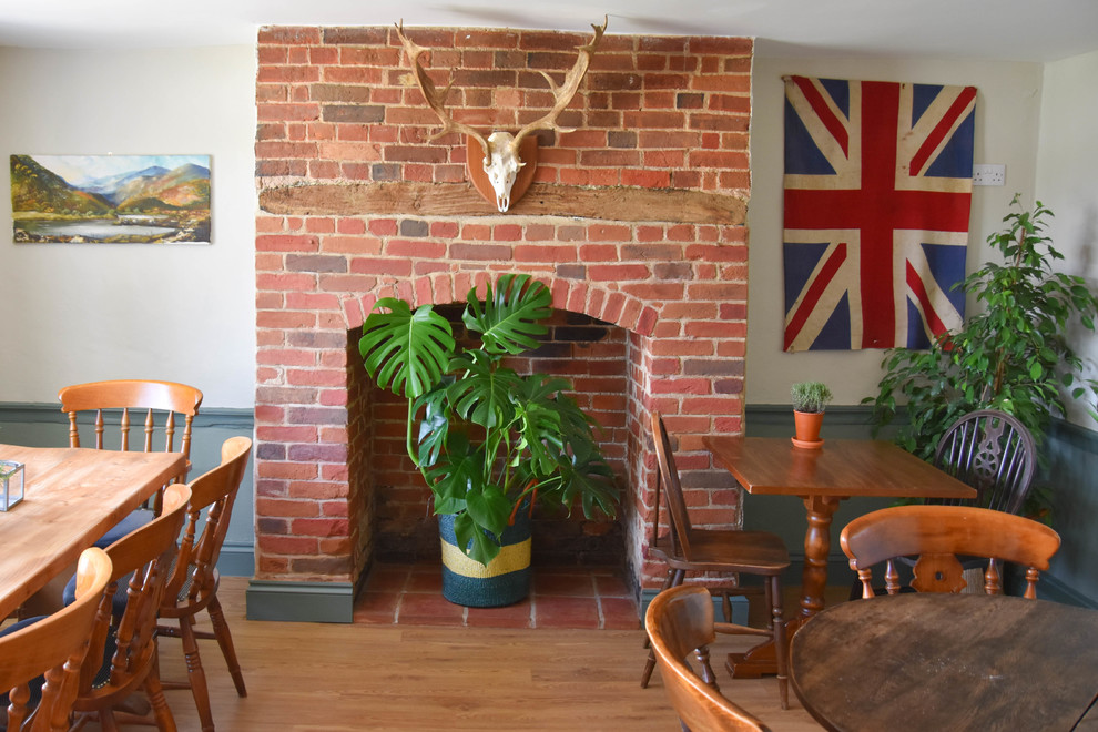 Mid-sized country separate dining room in Dorset with green walls, laminate floors, a standard fireplace, a brick fireplace surround and brown floor.