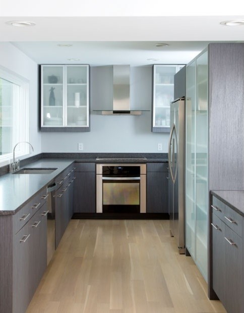 This is an example of a contemporary u-shaped kitchen in Boston with glass-front cabinets, grey cabinets, granite benchtops, stainless steel appliances, light hardwood floors and no island.