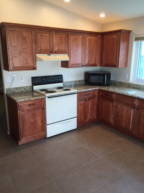 Example of a small transitional l-shaped ceramic tile eat-in kitchen design in Phoenix with an undermount sink, raised-panel cabinets, medium tone wood cabinets, granite countertops, white appliances and no island