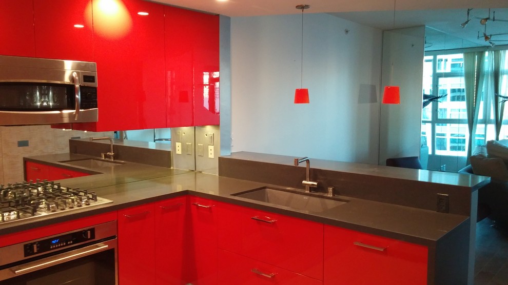 This is an example of a small modern u-shaped eat-in kitchen in San Diego with an undermount sink, flat-panel cabinets, red cabinets, quartz benchtops, metallic splashback, glass sheet splashback, stainless steel appliances, painted wood floors and a peninsula.