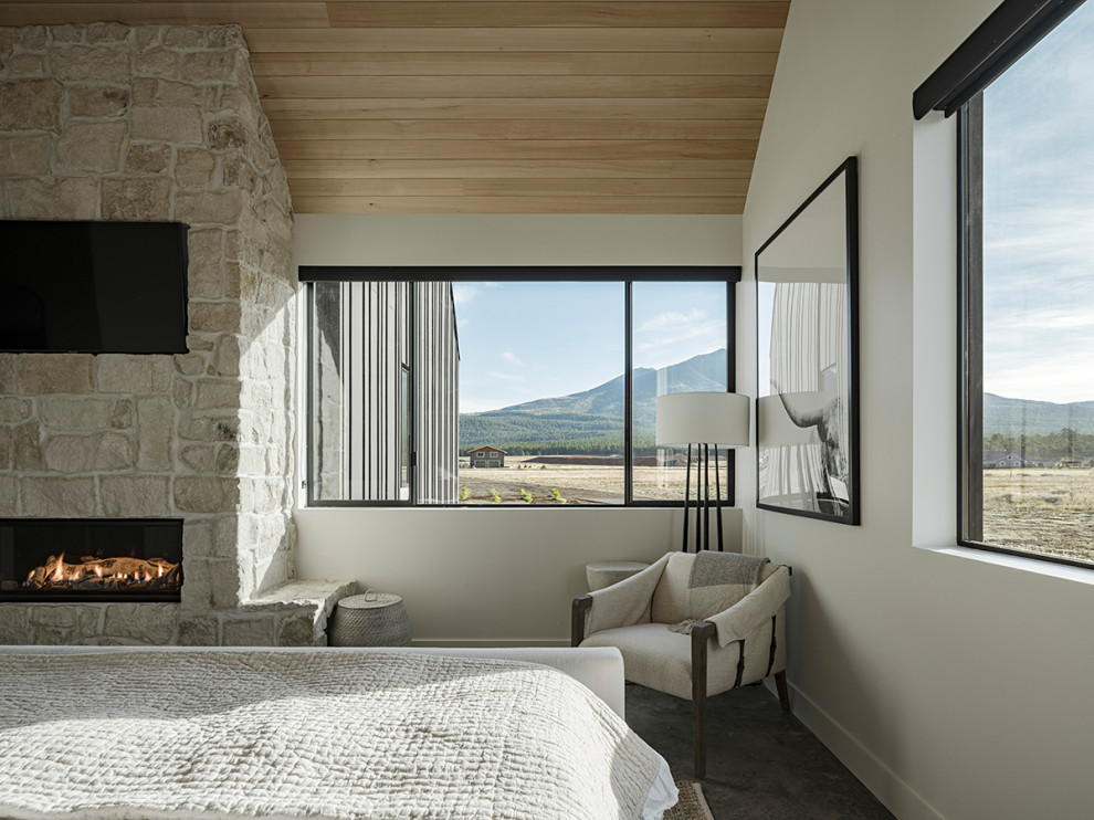 Example of a country master concrete floor, gray floor and vaulted ceiling bedroom design in Phoenix with white walls, a corner fireplace and a stone fireplace