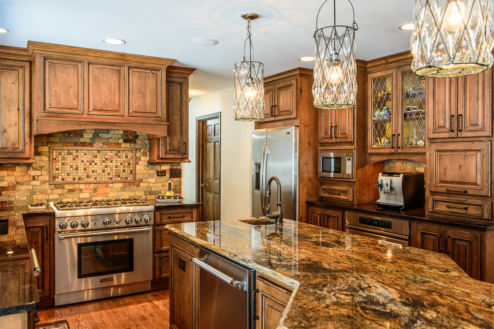 Example of a large mountain style kitchen design in Chicago with an undermount sink, raised-panel cabinets, granite countertops, stone tile backsplash, stainless steel appliances and an island