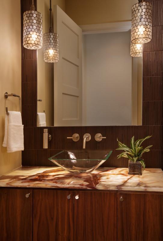 Inspiration for a contemporary powder room in Austin with onyx benchtops, brown tile, medium hardwood floors, flat-panel cabinets, medium wood cabinets, beige walls, a vessel sink, a two-piece toilet and beige floor.