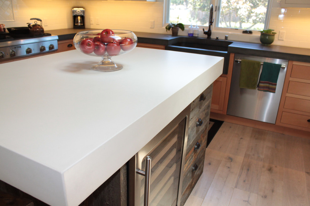 Photo of a contemporary u-shaped eat-in kitchen in San Francisco with a farmhouse sink, flat-panel cabinets, light wood cabinets, concrete benchtops, white splashback, ceramic splashback, stainless steel appliances and with island.