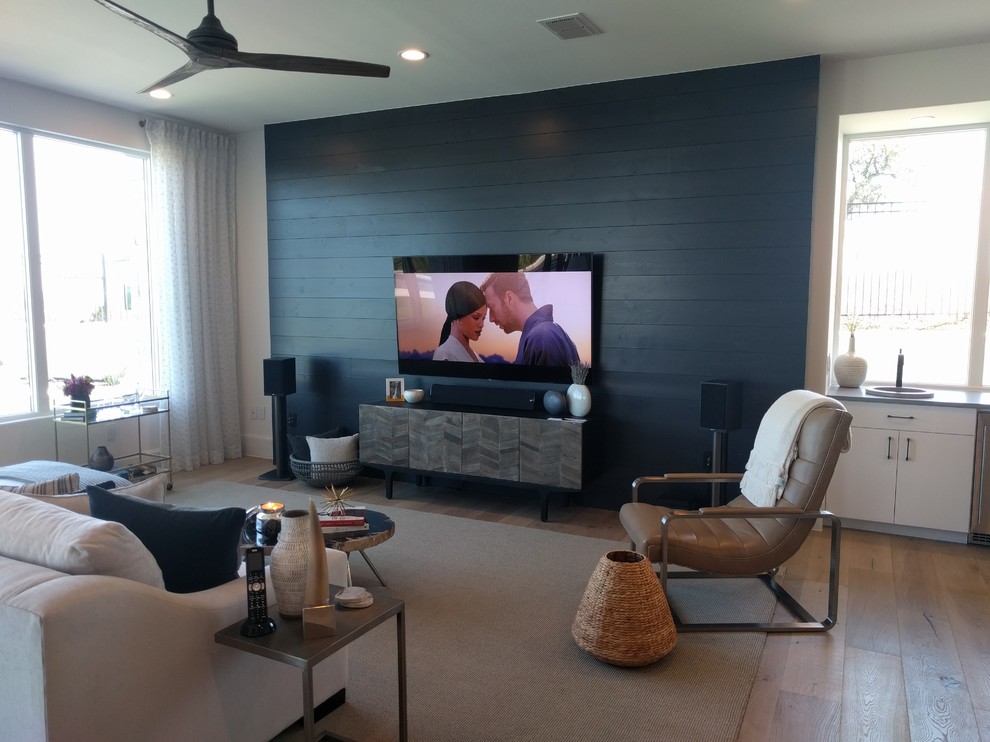 Large contemporary open concept home theatre in Austin with black walls, light hardwood floors, a wall-mounted tv and brown floor.