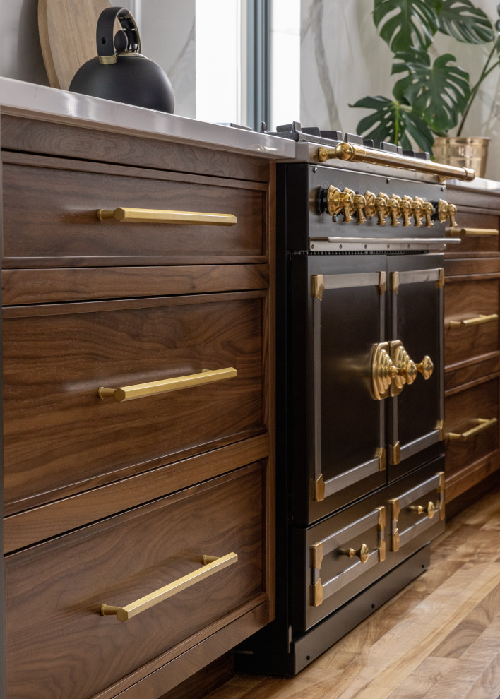 Mid-sized transitional l-shaped light wood floor and brown floor eat-in kitchen photo with a farmhouse sink, shaker cabinets, blue cabinets, quartz countertops, white backsplash, quartz backsplash, black appliances, an island and white countertops