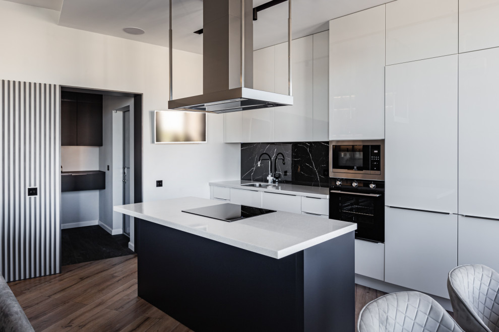 Exempel på ett mellanstort modernt vit linjärt vitt kök, med en undermonterad diskho, släta luckor, svart stänkskydd, stänkskydd i porslinskakel, svarta vitvaror, laminatgolv, en köksö och brunt golv